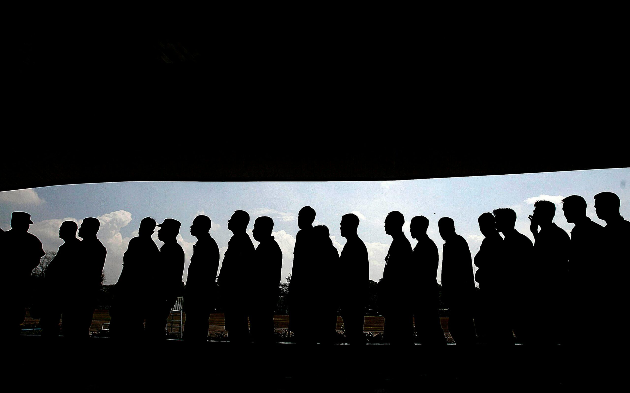 Silhouettes of people in line under a shaded canopy, highlighting social interaction and society.