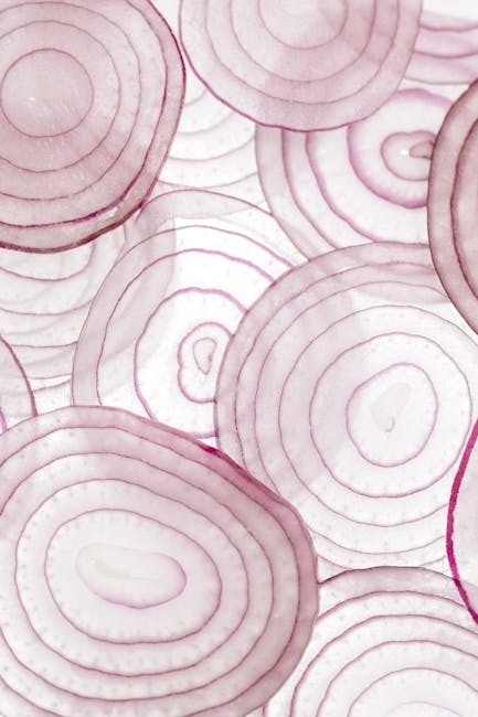 Detailed close-up of thinly sliced red onions arranged on a white surface, showcasing texture.